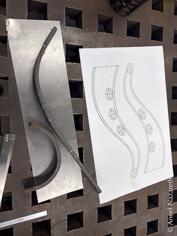 Two pieces of bar that have the desired curves are placed on a flat piece. Two copies of the tentacle shape are next to it to compare the curves.